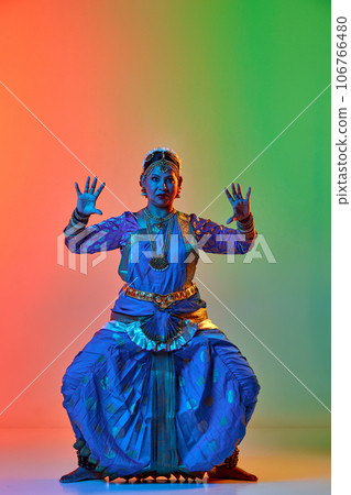 Elegant, artistic indian woman in traditional dress dancing against gradient studio background in neon light 106766480