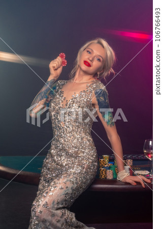 Blonde woman with a beautiful hairstyle and perfect make-up is posing with red gambling chips in her hands. Casino, poker. 106766493