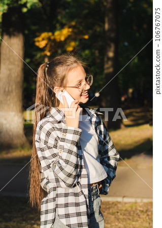 Cheerful girl in glasses talking on a dump phone outside vertical view Cheerful girl in glasses talking on a dump phone outside vertical view 106767075