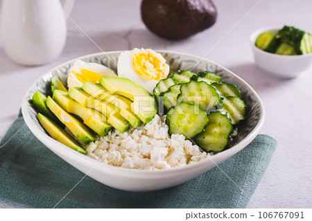 Bowl with cottage cheese, cucumber and avocado slices and boiled egg on the table 106767091