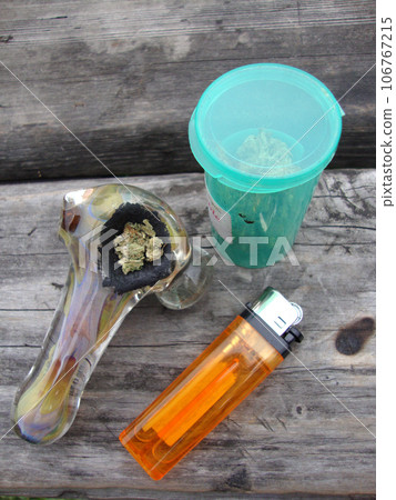 Jar of Medical Marajuana, Pipe and lighter sitting on a well used wood table 106767215