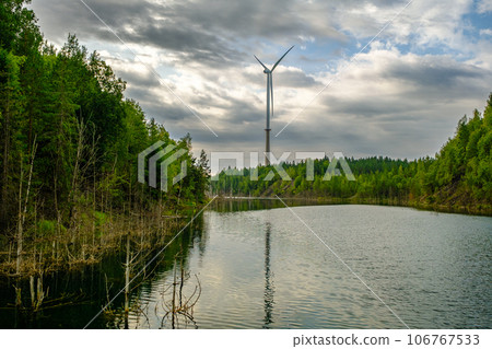 This is a former shale quarry with azure water and picturesque hills. Unlike the Narva shale settling ponds. A dark autumn day. Estonia, Aidu quarry. A tall wind turbine in the distance 106767533