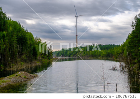 This is a former shale quarry with azure water and picturesque hills. Unlike the Narva shale settling ponds. A dark autumn day. Estonia, Aidu quarry. A tall wind turbine in the distance 106767535