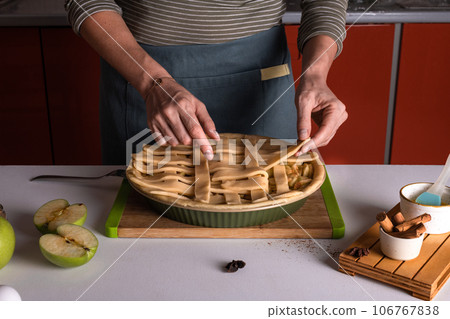 Woman placing pie dough on top of the apple pie in the bakery dish, decorating 106767838