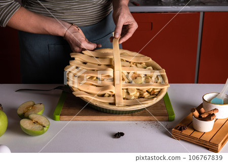 Woman placing pie dough on top of the apple pie in the bakery dish, decorating 106767839