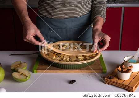 Woman placing pie dough on top of the apple pie in the bakery dish, decorating 106767842