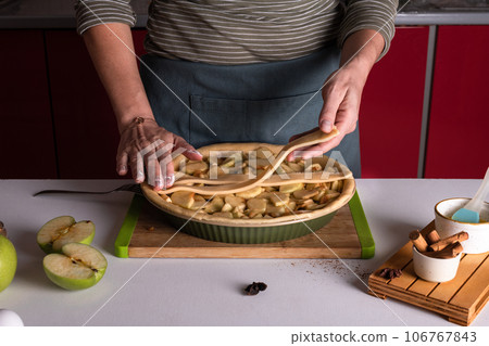 Woman placing pie dough on top of the apple pie in the bakery dish, decorating 106767843
