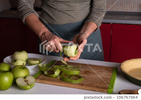 Woman is peeling apples to prepare apple pie in the kitchen. Authentic female hands peel an apple 106767864