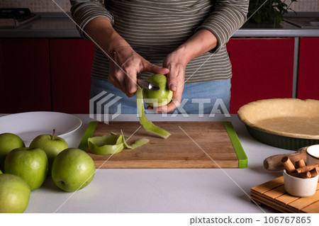 Woman is peeling apples to prepare apple pie in the kitchen. Authentic female hands peel an apple Woman is peeling apples to prepare apple pie in the kitchen. Authentic female hands peel an apple 106767865