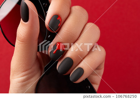 Close up womans hand with halloween manicure on red background holding sunglasses. Manicure, pedicure beauty salon concept 106768250
