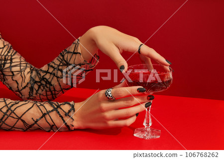 Womans hands with spooky nail design holding glass with cranberry halloween cocktail on red background Womans hands with spooky nail design holding glass with cranberry halloween cocktail on red background 106768262