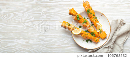 Grilled barbecue salmon skewers seasoned with green parsley and lemon on ceramic plate on white wooden rustic table background top view, healthy eating 106768282