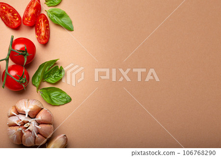 Food cooking border with cherry tomatoes, fresh green basil and garlic cloves top view on simple clean paper background, ingredients for preparing meal, copy space 106768290