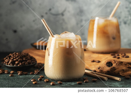 Ice coffee in a tall glass with cream poured over, ice cubes and beans on a dark concrete table. Ice coffee in a tall glass with cream poured over, ice cubes and beans on a dark concrete table. 106768507