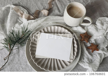 Christmas still life. Blank horizontal greeting card, invitation mockup. Scalloped plate. Wooden stars, pine tree branches. White linen tablecloth. Cup of coffee, winter breakfast. Flatlay, top view 106768601
