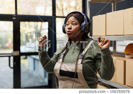 Stockroom manager listening music during work break, wearing headphones while working in storehouse. African american supervisor preparing customers orders working at shipping details 106768976
