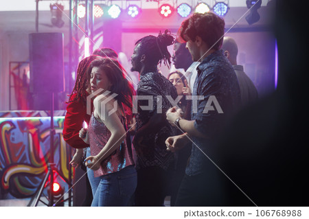 Young woman making passionate dance moves while clubbing with friends at discotheque. Crowd partying on vibrant dancefloor while attending disco party with live music in nightclub Young woman making passionate dance moves while clubbing with friends at discotheque. Crowd partying on vibrant dancefloor while attending disco party with live music in nightclub 106768988