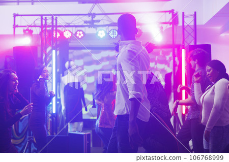 Young people dancing and partying on dancefloor at discotheque in nightclub. Diverse clubbers moving to music rhythm while having fun and celebrating in club with spotlights 106768999