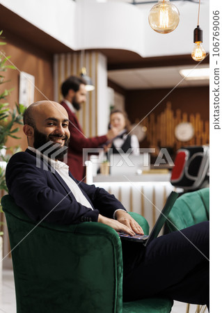 Guest prepares for business meeting, working on laptop in lounge area lobby before room registration. Businessman engaging in productive work to kill time while he waits for conference. 106769006