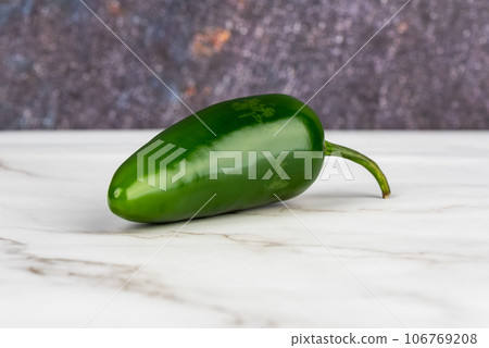 Close-up of a pod of green hot pepper on a light surface. Close-up of a pod of green hot pepper on a light surface. 106769208