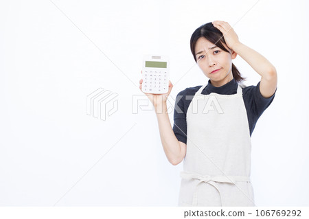 A housewife in her 30s holding a calculator and holding her head in front of a white background 106769292