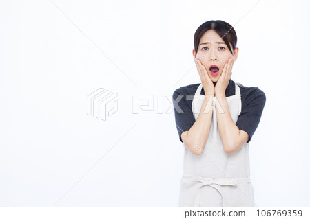 A housewife in her 30s looking surprised in front of a white background 106769359