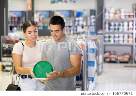 Husband buyer with paint container in hand consults with wife and examines can of enamel dye 106770671