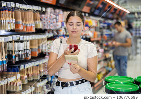 Female shopper scans QR code with her phone to check product information. Buying paint brushes at hardware store Female shopper scans QR code with her phone to check product information. Buying paint brushes at hardware store 106770689