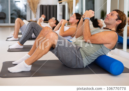 Active vigorous man performs exercises with a pilates roller while on a mat in the hall of a modern fitness studio. 106770778