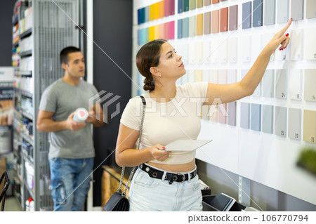 Near stand with samples paint, palette of colors of coating, woman buyer examines showcase 106770794