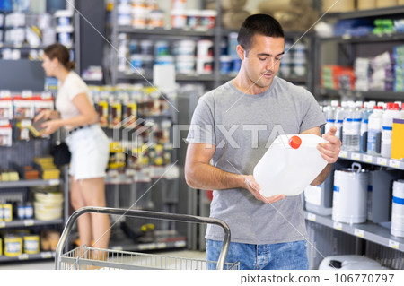 Interested young handyman choosing quality paint primer in store 106770797