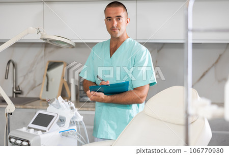 Portrait shot of male doctor holding clipboard in hand while standing in medical esthetic clinic Portrait shot of male doctor holding clipboard in hand while standing in medical esthetic clinic 106770980