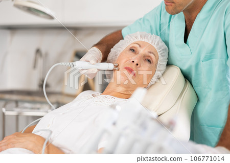 Elderly female client receiving hardware ultrasonic to revitalize and tighten facial skin at cosmetology clinic 106771014