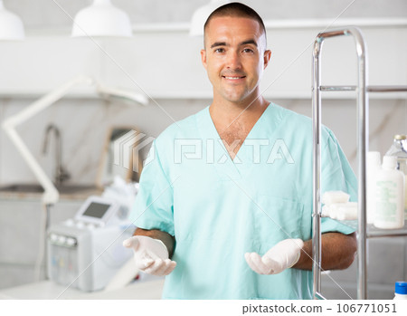 Portrait of male doctor cosmetologist wearing overall showing equipment of clinic before procedure Portrait of male doctor cosmetologist wearing overall showing equipment of clinic before procedure 106771051