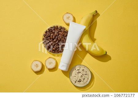 Glass petri dishes containing roasted coffee beans and mixture of banana and coffee substances. Top view. Empty label tube for cosmetic product mockup design 106772177
