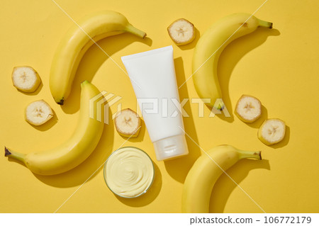 Banana cut in slices are arranged with white tube and a petri dish of cosmetic cream on yellow background. Banana (Musaceae) can help reduce fine lines and wrinkles Banana cut in slices are arranged with white tube and a petri dish of cosmetic cream on yellow background. Banana (Musaceae) can help reduce fine lines and wrinkles 106772179
