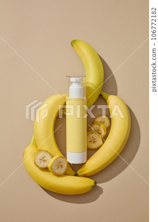 Cosmetic bottle in yellow color is decorated with several fresh bananas. Beige background. Banana (Musaceae) is one of the most widely consumed fruits on the planet Cosmetic bottle in yellow color is decorated with several fresh bananas. Beige background. Banana (Musaceae) is one of the most widely consumed fruits on the planet 106772182