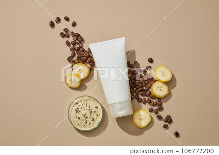 An empty label tube decorated with roasted coffee beans and banana slices. Petri dish of cream texture featured. Banana and coffee can be a great scrub for skin An empty label tube decorated with roasted coffee beans and banana slices. Petri dish of cream texture featured. Banana and coffee can be a great scrub for skin 106772200