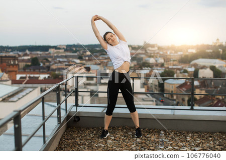 Young person raising hands in stretches on city background 106776040