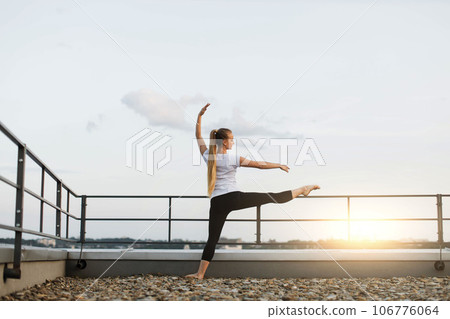 Person stretching leg muscles on roof handrails at sunset 106776064