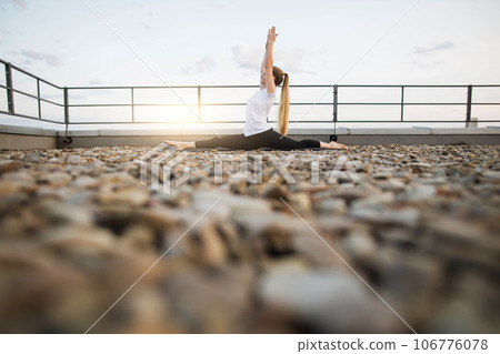 Female performing front split on mat in outdoor yoga session 106776078