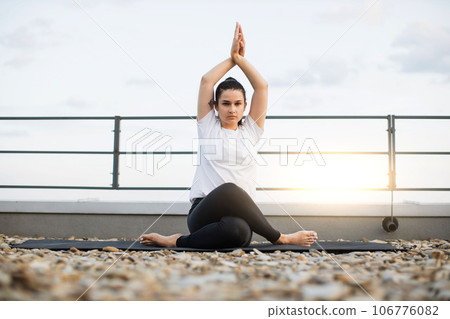 Woman taking up seated posture on roof terrace at sunset 106776082