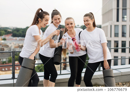Sporty ladies clinking water bottle after yoga class on roof 106776679