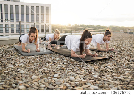 Women doing forearm plank on yoga mats in open air on roof Women doing forearm plank on yoga mats in open air on roof 106776702