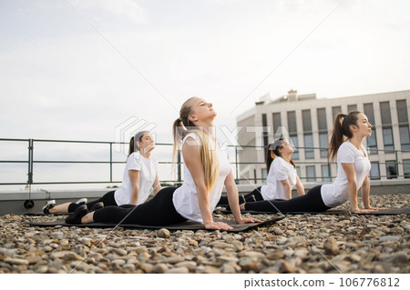 Ladies doing spinal extension during outdoor yoga session Ladies doing spinal extension during outdoor yoga session 106776812