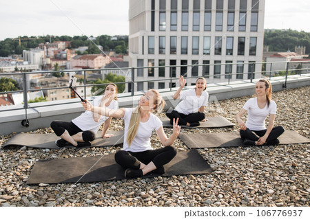 Ladies posing at phone on selfie stick during outdoor yoga 106776937