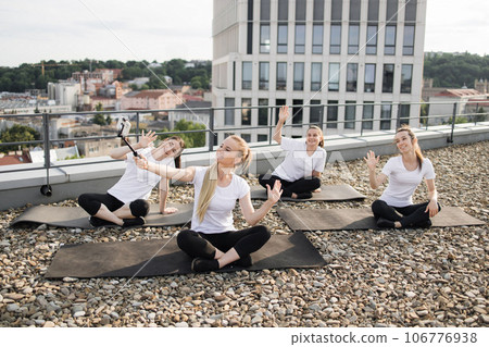 Ladies posing at phone on selfie stick during outdoor yoga 106776938