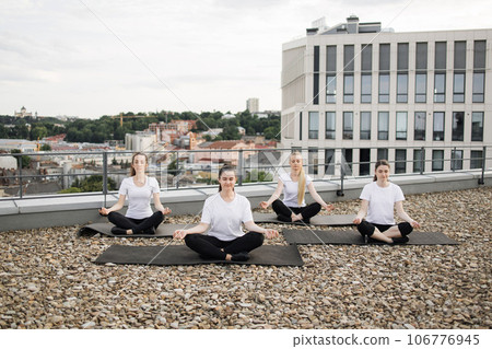Women exercising lotus pose with gyan mudra on rooftop 106776945