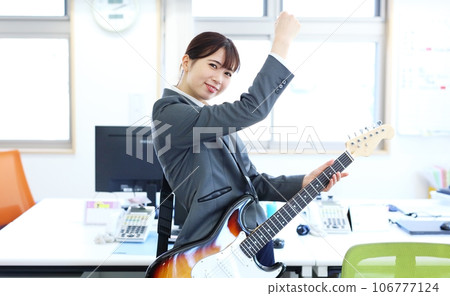 Image of a female office worker playing an electric guitar at work Image of a female office worker playing an electric guitar at work 106777124