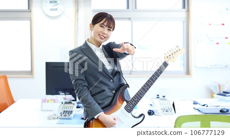 Image of a female office worker playing an electric guitar at work 106777129